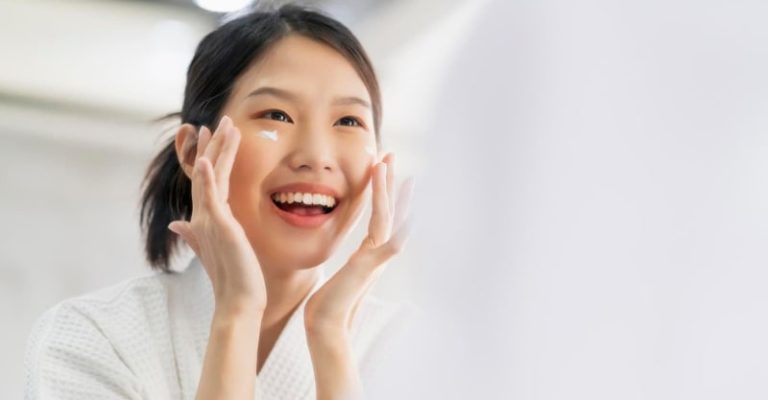 一名笑容燦爛的女子在鏡子前塗抹保養品，展現護膚步驟與日常皮膚保養。